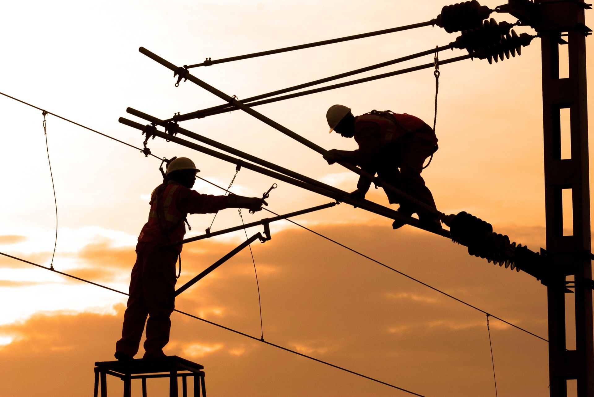 Two linemen working high on utility poles against a clear sky