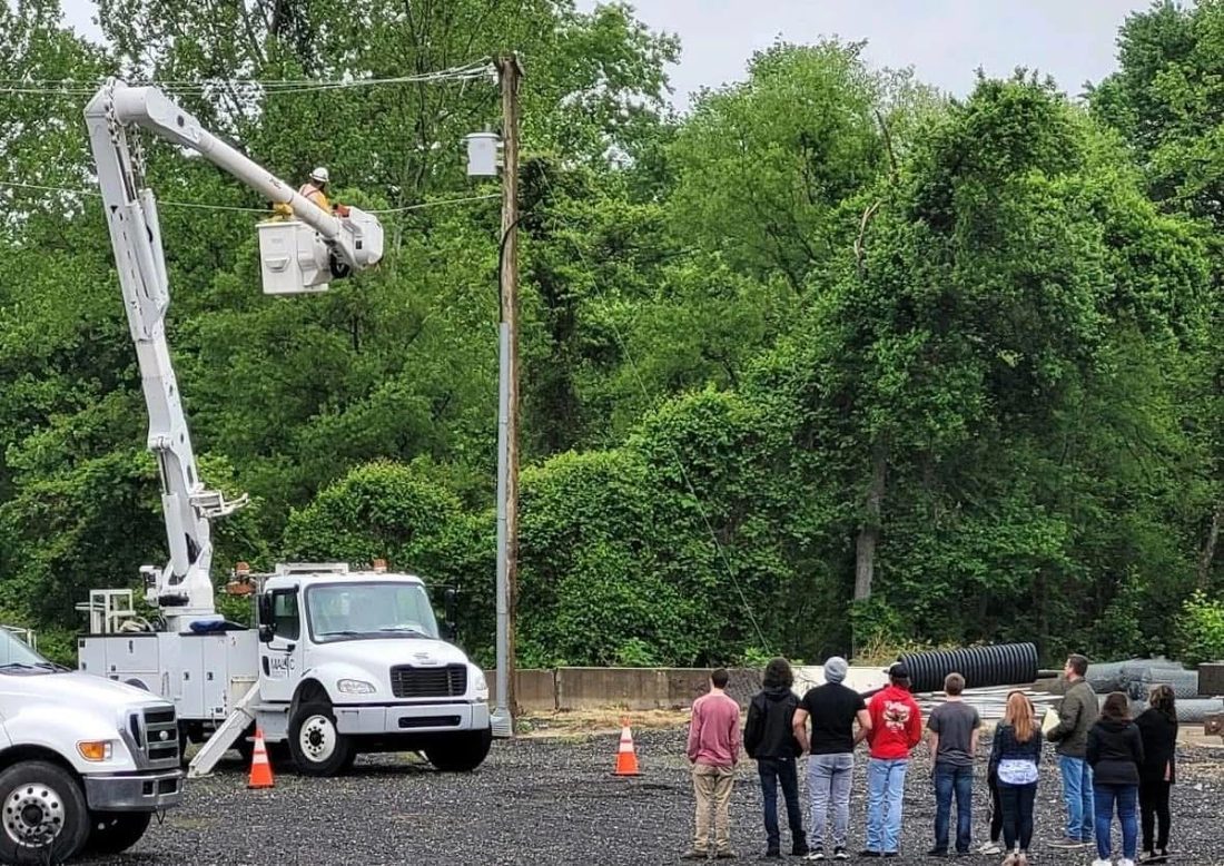 An instructor in an aerial bucket demonstrating pole work to a class of lineman trainees